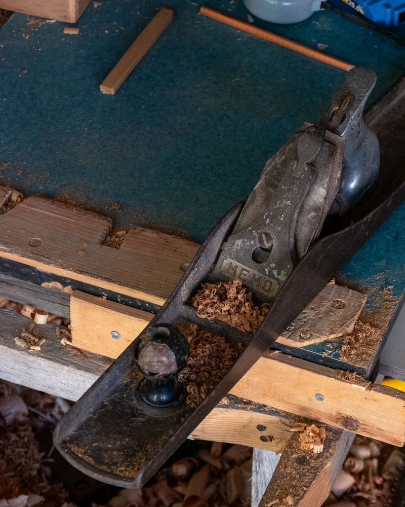 Cepillo de mano metálico apoyado sobre un banco de taller entre virutas rizadas de madera